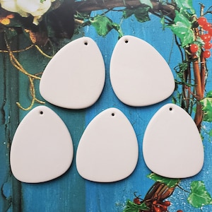 May include: Five off-white, teardrop-shaped ceramic pendants with a small hole at the top for stringing. The pendants have a smooth, matte finish and are arranged against a blue and green background with floral and vine accents.
