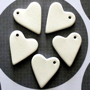 May include: Five white ceramic heart-shaped ornaments with a hole at the top for hanging.