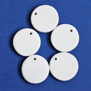 May include: Five white ceramic round ornaments with a small hole at the top. The ornaments are arranged in a circle on a blue background.