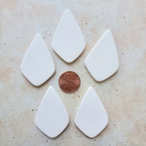 May include: Five white ceramic teardrop-shaped pendants, each about the size of a US penny.
