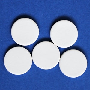 May include: Five white round ceramic coasters on a blue background.