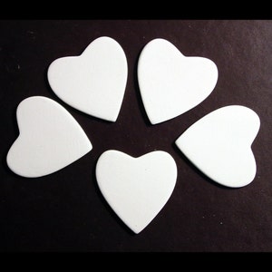 May include: Five white heart-shaped ceramic tiles, arranged in a circle on a black background.