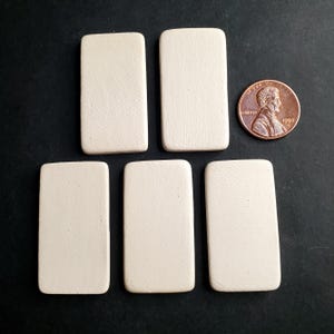 May include: Five rectangular, off-white, smooth-surfaced tiles arranged in a group. A copper-colored United States one-cent coin is positioned to the right of the top-right tile for scale, showing the profile of Abraham Lincoln.