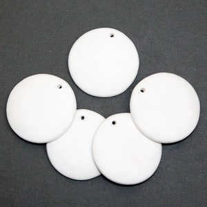 May include: Five circular white ornaments, each featuring a single small hole near the top edge for hanging. These smooth, matte-finished discs are arranged in a cluster, presenting a clean, uniform appearance suitable for various craft projects.