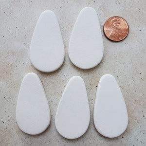 May include: Five white ceramic teardrop-shaped pendants, each about the size of a US penny.