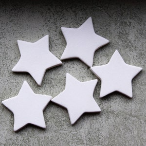 May include: Five white star-shaped ornaments arranged on a textured gray surface. Each star has five points and a slightly rounded shape. The stars are evenly spaced, creating a decorative arrangement.