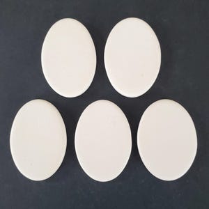 May include: Five smooth, solid white oval-shaped pieces arranged in a pattern with two pieces on the top row and three pieces on the bottom row. Each piece has a flat, matte surface and rounded edges, presenting a uniform and simple appearance.
