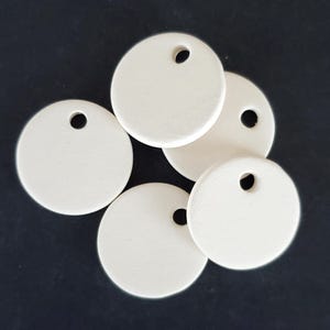 May include: Five circular, off-white, matte-finished discs arranged in a cluster. Each disc features a single, small, circular hole punched near the top edge, providing a consistent design across all five pieces for various craft applications.
