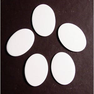 May include: Five white oval-shaped ceramic tiles arranged in a starburst pattern on a dark brown background.