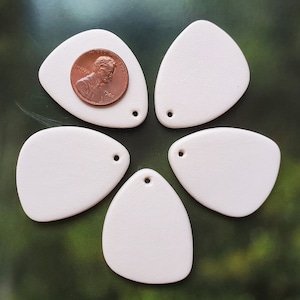 May include: Five white ceramic pendants shaped like teardrops with a hole at the top. The pendants are arranged in a flower shape with a penny in the center.