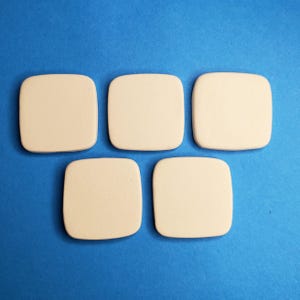 May include: Five smooth, square-shaped tiles with rounded corners, featuring a solid, light beige, matte finish. The tiles are arranged in a pattern with three across the top and two centered below, presenting a uniform, flat surface.