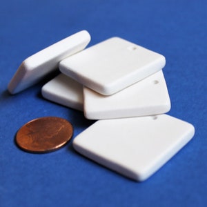 May include: Four white ceramic square tiles with a hole in the top corner. The tiles are stacked on top of each other. A penny is in the foreground.
