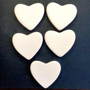 May include: Five white ceramic heart-shaped ornaments. The hearts are smooth and have a slightly textured surface.