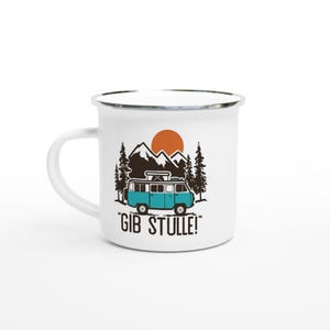 以下が含まれることがあります： 白いエナメルマグ。黒とターコイズブルーのキャンピングカー、山、木、太陽のイラスト。テキスト「GIB STULLE！」が下に印刷されています。マグにはシルバーのリムと白いハンドルが付いています。