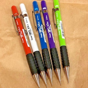 May include: Five Pentel 120 A3DX mechanical pencils in red, white, blue, purple, and green. Each pencil has a black grip, a silver clip, and the text "Pentel 120 A3DX" and "A315 JAPAN". The pencils have different lead sizes.