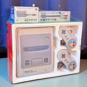 Peut inclure: Un ensemble de console de jeu Nintendo Super Famicom dans son emballage d'origine, comprenant une console gris clair, deux manettes grises avec des boutons multicolores, une boîte d'adaptateur secteur HVC-002 et un câble S-terminal SHVC-009.