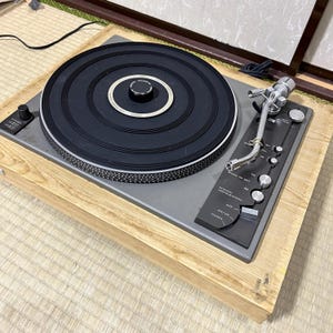 Może przedstawiać: Zabytkowy gramofon z czarną płytą i srebrnym ramieniem. Gramofon ma drewnianą podstawę i panel sterowania z przyciskami i przełącznikami. Zaprojektowany do odtwarzania płyt winylowych.