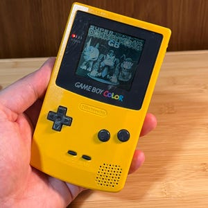 Könnte beinhalten: Gelbe Game Boy Color Handheld-Konsole mit einem Spiel auf dem Bildschirm. Die Konsole hat ein Steuerkreuz, Knöpfe und die Aufschrift "GAME BOY COLOR" und "Nintendo". Das Spiel auf dem Bildschirm ist "Super Donkey Kong GB".