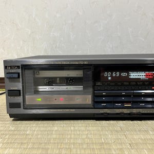 Könnte beinhalten: Ein silber-schwarzer Stereo-Kassettenrekorder, Modell FD-90, mit eingelegter Kassette. Das Gerät verfügt über eine Digitalanzeige mit der Anzeige "00 69" und verschiedene Bedientasten. Die Marke "TOA" ist auf der linken Seite sichtbar.