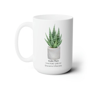 Pode incluir: Caneca de cerâmica branca com uma ilustração de planta cobra verde e o texto "Snake Plant /'sna:k(ǝ)//pla:nt/ Dracaena trifasciata" impresso nela.