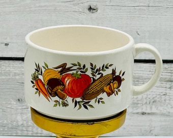 May include: White ceramic mug with a colorful vegetable design. The mug is on a gold stand.