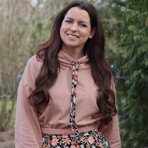 Pode incluir: Uma mulher vestindo um moletom rosa cropped com um cordão de ajuste de estampa floral e uma saia preta de estampa floral.