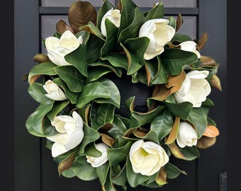 Könnte beinhalten: Ein weißer Magnolienkranz mit grünen Blättern. Der Kranz besteht aus künstlichen Blumen und Blättern.