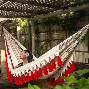 Colombian Luxury hammock for indoor and outdoor use and decor. Red and white handmade hammock featuring intricate crochet fringes with pom poms, perfect for adding a pop of color and artisanal charm to any space.