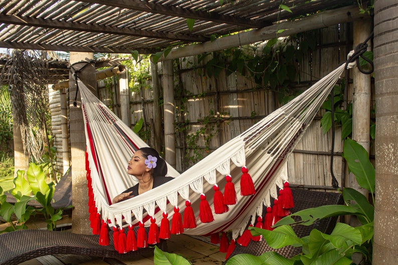 Colombian Luxury hammock for indoor and outdoor use and decor. Red and white handmade hammock featuring intricate crochet fringes with pom poms, perfect for adding a pop of color and artisanal charm to any space.