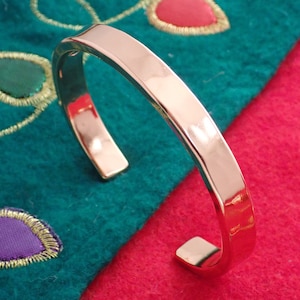 May include: A silver metal cuff bracelet with a smooth, polished finish. The bracelet is open and has a slightly squared shape.