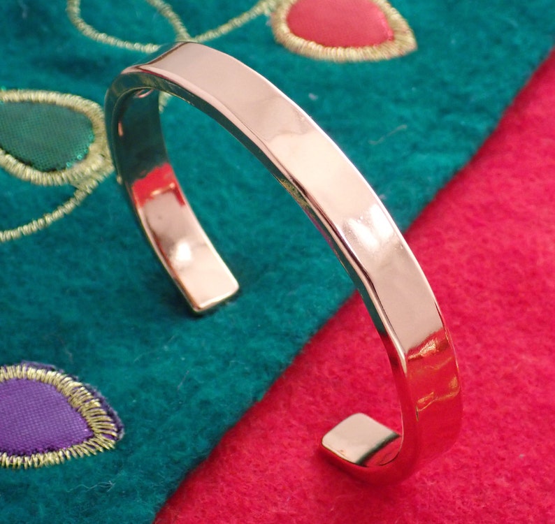 May include: A silver metal cuff bracelet with a smooth, polished finish. The bracelet is open and has a slightly squared shape.