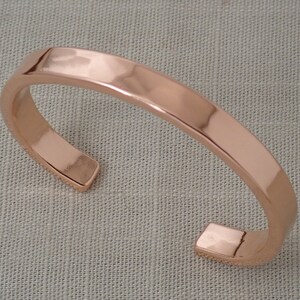May include: A simple, polished copper cuff bracelet. The bracelet is a solid band of copper with rounded edges.