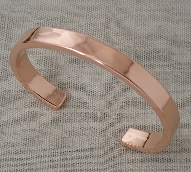 May include: A simple, polished copper cuff bracelet. The bracelet is a solid band of copper with rounded edges.