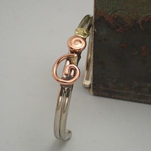 May include: A silver bangle bracelet with a copper swirl design and gold accents.