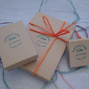 May include: Three brown cardboard boxes with the text "Northwest Goods" and "Hand Crafted Jewelry" printed on them. The boxes are tied with orange string and a bow.