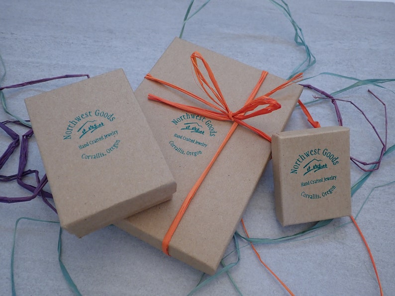 May include: Three brown cardboard boxes with the text "Northwest Goods" and "Hand Crafted Jewelry" printed on them. The boxes are tied with orange string and a bow.