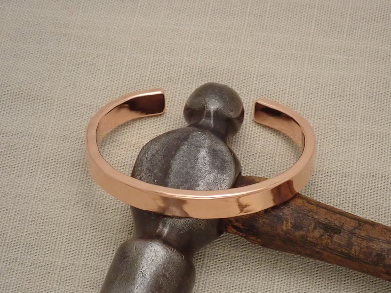 May include: A copper bracelet with a smooth, polished finish. The bracelet is open and has a slightly rounded shape.