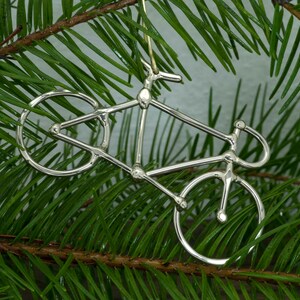 May include: Silver bicycle ornament hanging from a green pine tree branch.