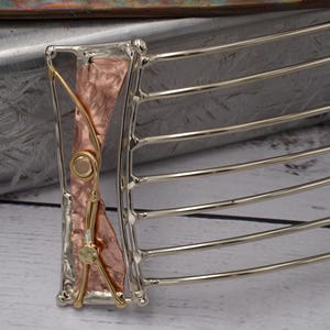 May include: A hair comb featuring a silver-toned frame with seven curved tines. The decorative head of the comb displays a central vertical panel of hammered copper, accented with thin, polished gold-toned wire detailing and two small circular studs.