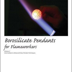 Puede incluir: Primer plano de un colgante de vidrio que se calienta con un soplete. El colgante es un patrón de vidrio rojo y blanco en espiral. El texto "Borosilicate Pendants for Flameworkers" es visible en la parte inferior de la imagen. El texto "Volume 2 Intermediate to Advanced Glass Pendant Techniques" también es visible.