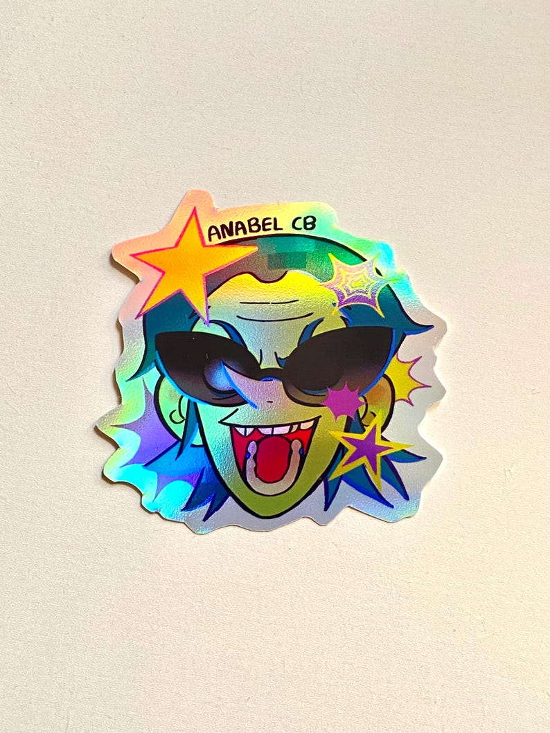 May include: Holographic sticker featuring a cartoon face with sunglasses, a wide open mouth, and spiky hair. The sticker has a star and the text "ANABEL CB". The sticker has a rainbow effect.