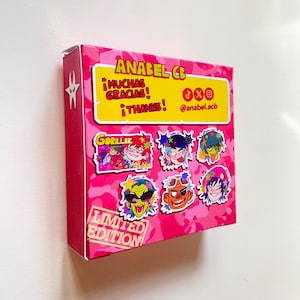 May include: A pink box with a camouflage pattern and the text "ANABEL CB" in yellow. The box features cartoon character stickers and the words "&iexcl;MUCHAS GRACIAS! &iexcl;THANKS!" in yellow. The words "LIMITED EDITION" are also visible.