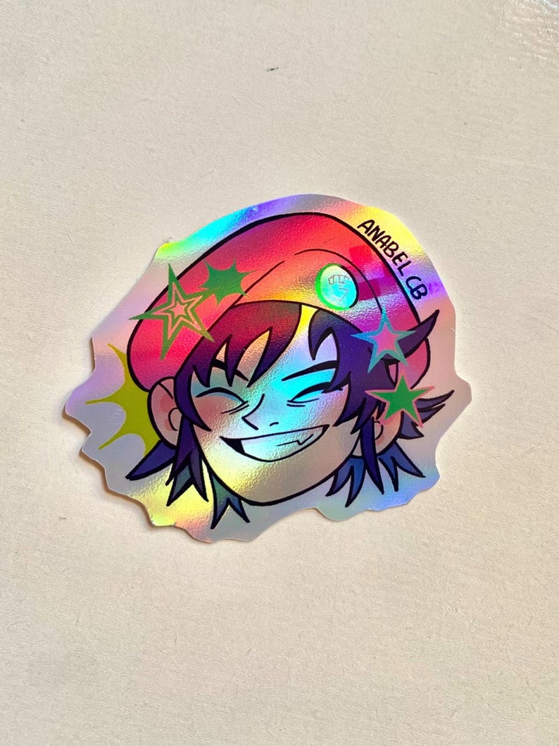 May include: Holographic sticker featuring a smiling cartoon character with purple hair and a pink hat. The sticker has green and purple star accents and the text "ANABEL CB". The sticker has a shiny, iridescent finish.