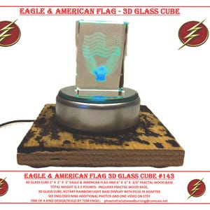 May include: A 3D glass cube with an eagle and American flag design on a rotating base. The base is made of wood and has a fractal pattern. The cube is illuminated from below, creating a rainbow effect. The text "EAGLE & AMERICAN FLAG 3D GLASS CUBE #143" is visible below the cube.