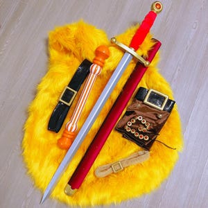 May include: A cosplay set featuring a silver sword with a red handle and scabbard, a black belt, a brown pouch, and a beige belt. The items are arranged on a yellow faux fur surface. The sword has a gold crossguard.