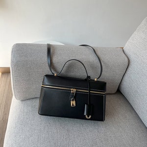 May include: A black leather handbag with a gold zipper and lock. The bag has a top handle and a shoulder strap.