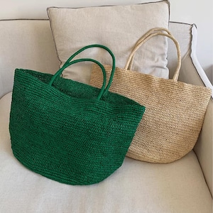 May include: Two woven tote bags. One is emerald green, the other is natural beige. Both have matching handles. The bags are made of a textured material and are sitting on a white surface.