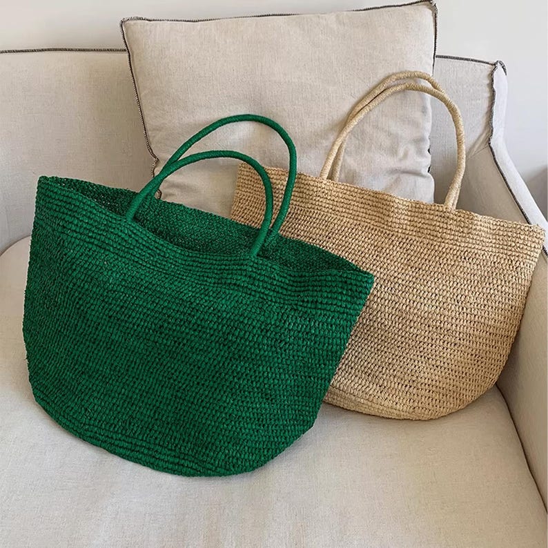 May include: Two woven tote bags. One is emerald green, the other is natural beige. Both have matching handles. The bags are made of a textured material and are sitting on a white surface.