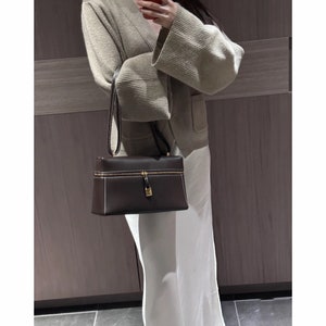 May include: A brown leather handbag with a gold zipper and lock. The bag has a rectangular shape and a top handle.