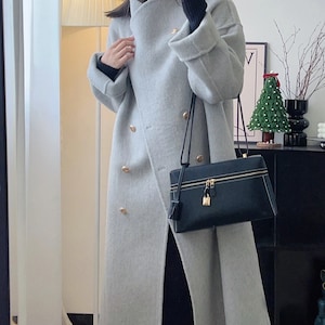 May include: A gray double-breasted wool coat with gold buttons and a black leather crossbody bag with a gold zipper and lock.